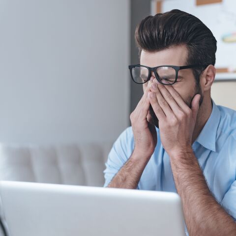 Un homme est assis devant un ordinateur et se frotte les yeux