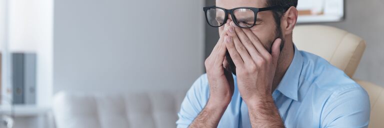 Mann sitzt am Computer und reibt sich die Augen