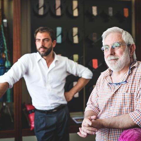 Deux hommes dans un magasin se tiennent côte à côte, l’un à l’arrière-plan portant une chemise et l’autre au premier plan portant des lunettes et une chemise à carreaux.