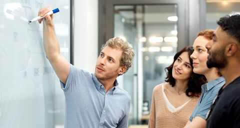Young employees have a meeting and stand at a whiteboard.