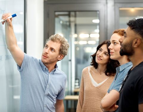 I giovani collaboratori hanno una riunione e si trovano a una whiteboard. 