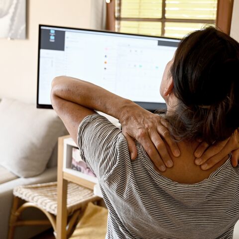 Une personne est assise devant un écran d’ordinateur et se masse la nuque, probablement en raison de tensions ou de douleurs.