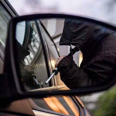 Dans le rétroviseur latéral d'une voiture, on aperçoit un homme cagoulé qui tente de forcer la voiture