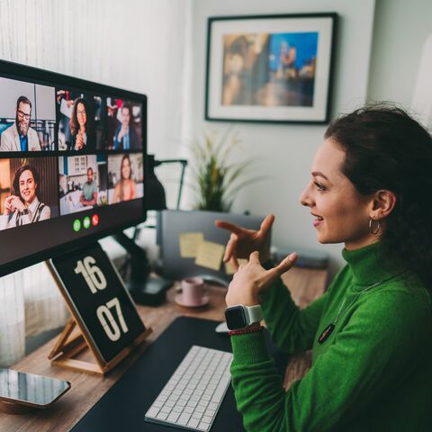 Une jeune femme portant un pull vert participe à une réunion Teams chez elle.