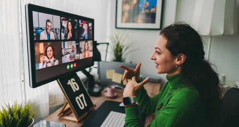 A young woman in a green jumper is taking part in a team meeting from home.