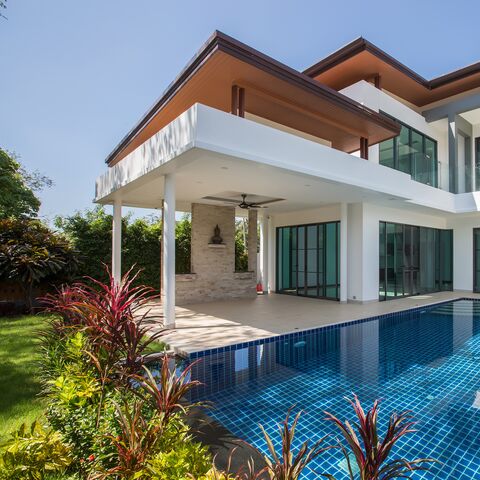 Eine moderne, grosszügige Villa mit Terrasse, grossen Fenstern und einem blau schimmernden Swimmingpool.