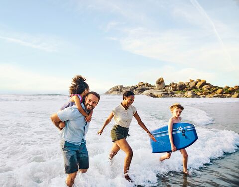 Une famille joyeuse se promène sur la plage. Le père porte l'enfant sur ses épaules, tandis que la mère marche à côté de lui en riant.
