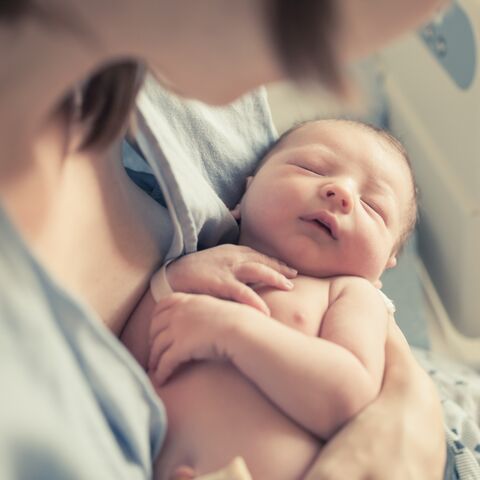 A mother gently holds her newborn baby in her arms while the baby sleeps quietly with its eyes closed.