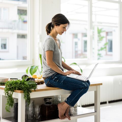 Une jeune femme est assise sur une table et regarde son ordinateur portable.