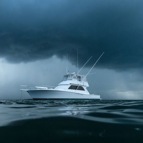 A white motor yacht is anchored in the dark sea. A storm is brewing in the background.