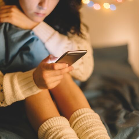 Frau sitz auf dem Bett und ist am Handy 