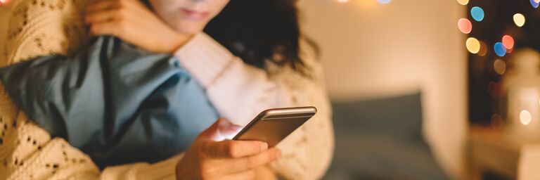 La donna è seduta sul letto e sta parlando al cellulare 