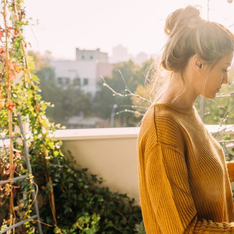 Eine Frau steht in der Sonne auf ihrem Balkon und kümmert sich um ihre Pflanzen.