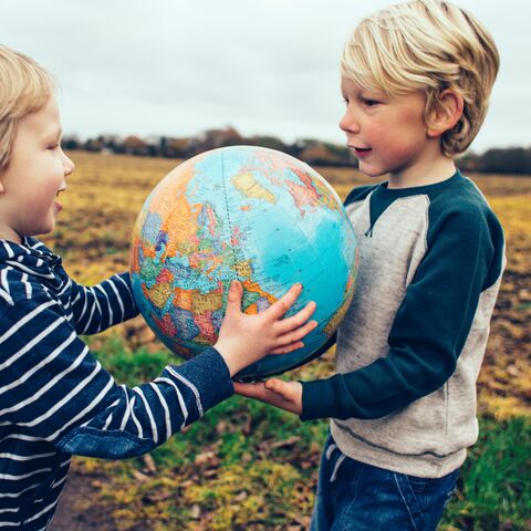 Deux enfants souriants se tiennent dans un champ et tiennent ensemble un globe tout en se regardant.