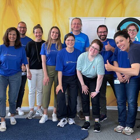 Team stands together and smiles at the camera. They are wearing blue AXA heart-to-heart T-shirts.