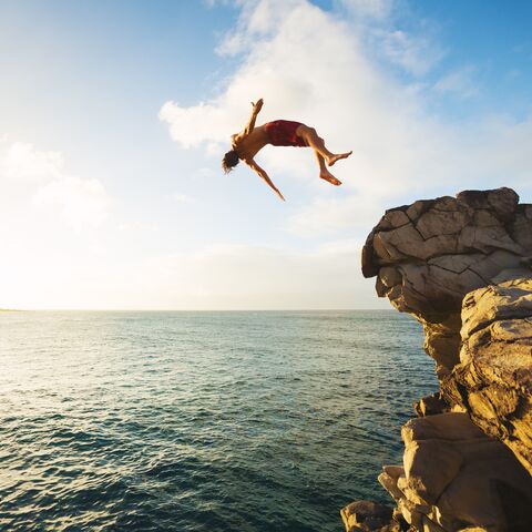 Ein Mann springt von einem Felsen ins Meer und macht dabei einen Rückwärtssalto