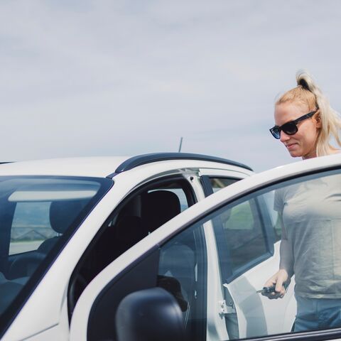 Eine blonde Frau mit Sonnenbrille öffnet die Tür eines weissen Autos und hält den Autoschlüssel in der Hand.