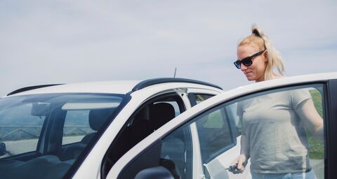 Eine blonde Frau mit Sonnenbrille öffnet die Tür eines weissen Autos und hält den Autoschlüssel in der Hand.