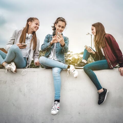 Trois jeunes femmes sont détendues sur un mur, rient et regardent un smartphone tout en écoutant de la musique.