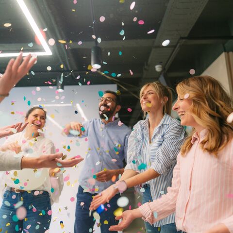 Des collaborateurs et une collaboratrice font la fête avec des confettis dans un bureau.