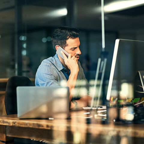 Un uomo in ufficio è seduto davanti a un computer e telefona