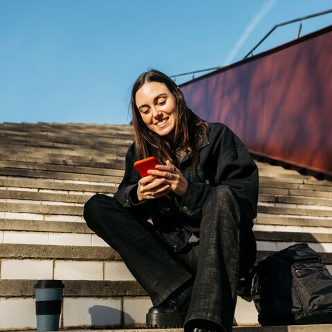 Una giovane donna è fuori su una scala e guarda il cellulare.