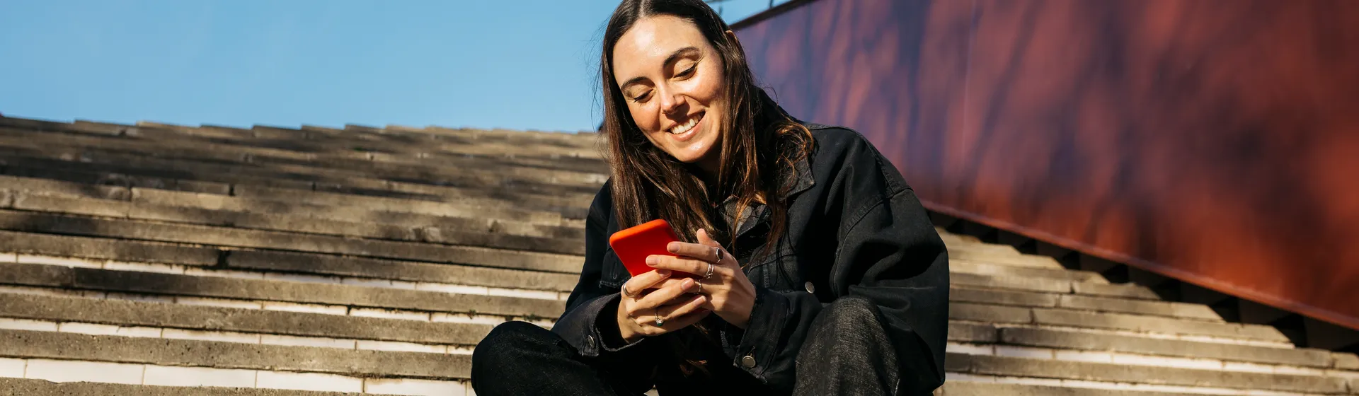 A young woman is outside on a staircase looking at her cell phone.