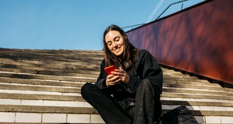 Une jeune femme est dans un escalier et regarde son téléphone portable.