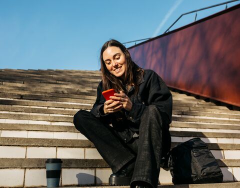 Une jeune femme est dans un escalier et regarde son téléphone portable.