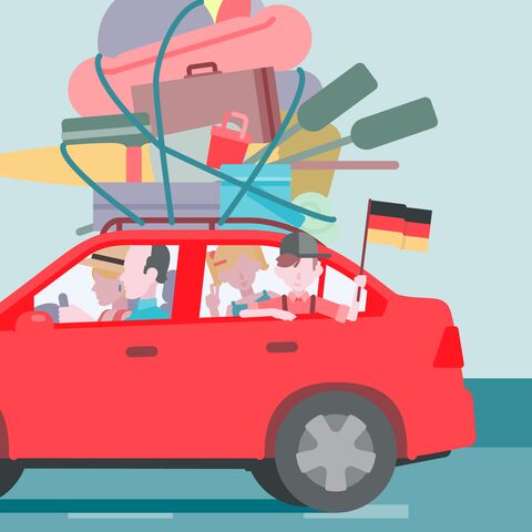 Una famiglia viaggia in un’auto rossa con molti bagagli sul tetto, davanti alla silhouette di Berlino con la torre della televisione sullo sfondo.