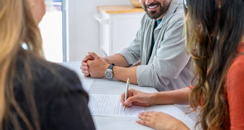 A young woman sits at a table with her parents and signs her apprenticeship contract.