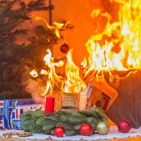 Ein Weihnachtsbaum brennt neben einem Kamin, Geschenke und Dekorationen sind in Flammen, verursacht durch Kerzen und Lichter.