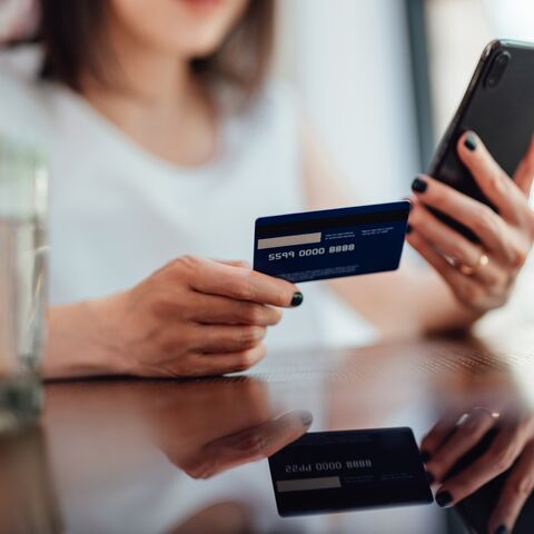 A woman holds a credit card in one hand and a smartphone in the other while sitting at a table.