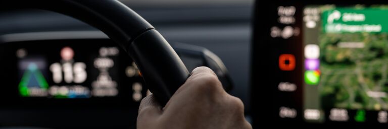 Elektroauto von innen, Frau hat Hand am Steuer, Navi ist sichtbar