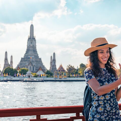 Junge Frau macht ein Selfi vor einem Tempel in Thailand.