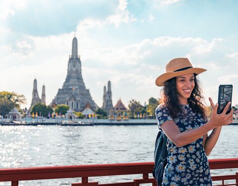 Junge Frau macht ein Selfi vor einem Tempel in Thailand.