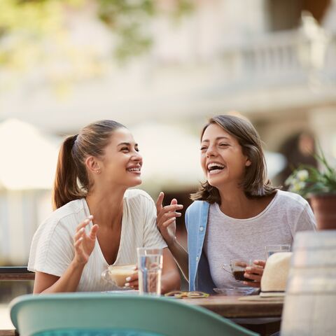 Two young women are sitting in a café, laughing together.