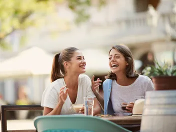 Two young women are sitting in a café, laughing together.