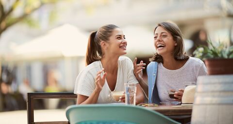 Zwei junge Frauen sitzen in einem Café und lachen miteinander.