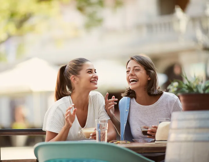 Two young women are sitting in a café, laughing together.
