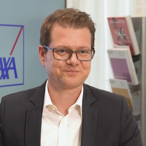 Ein Mann mit Brille und Anzug steht im Eingangsbereich einer AXA Agentur.