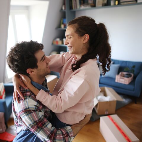 Ein junges paar befindet sich im Wohnzimmer und im Hintergrund sind Umzugskisten zu sehen.