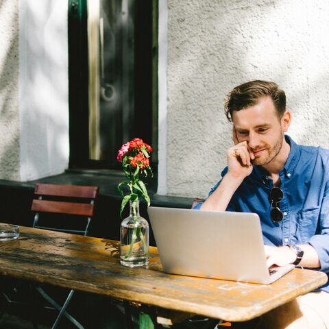 Ein Mann arbeitet an seinem Laptop draussen am Gartentisch.