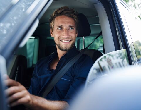 A young couple stand in front of a car smiling.