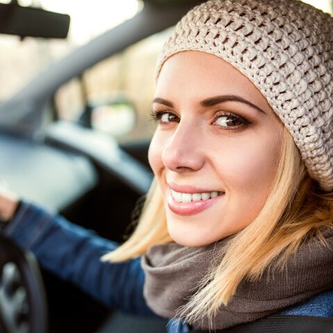 A young woman with blond hair and a knitted hat smiles out of the car window.