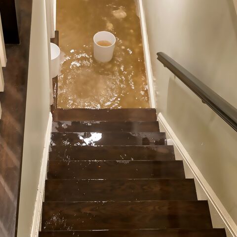 Un escalier de la cave mène à une cave inondée. Une chaudière blanche se trouve dans l’eau.
