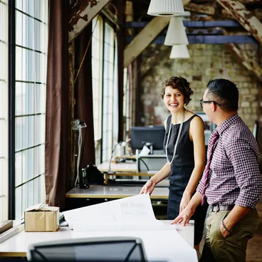 Collaboratrice souriante discutant avec un collègue à son poste de travail au bureau.