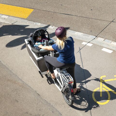 Una donna trasporta un bambino in un marsupio su una bicicletta cargo.