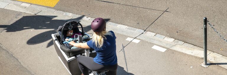 Una donna trasporta un bambino in un marsupio su una bicicletta cargo.