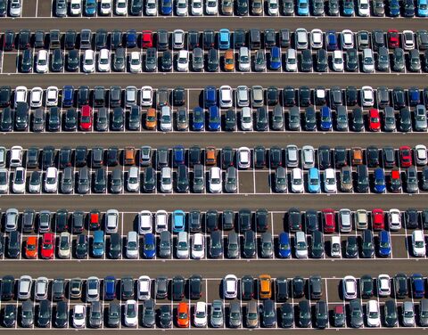 Veduta aerea di un ampio parcheggio con auto affiancate di diversi colori, disposte in file parallele.